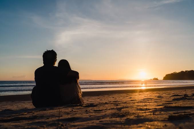 Casal observando o pôr do sol, de mãos dadas